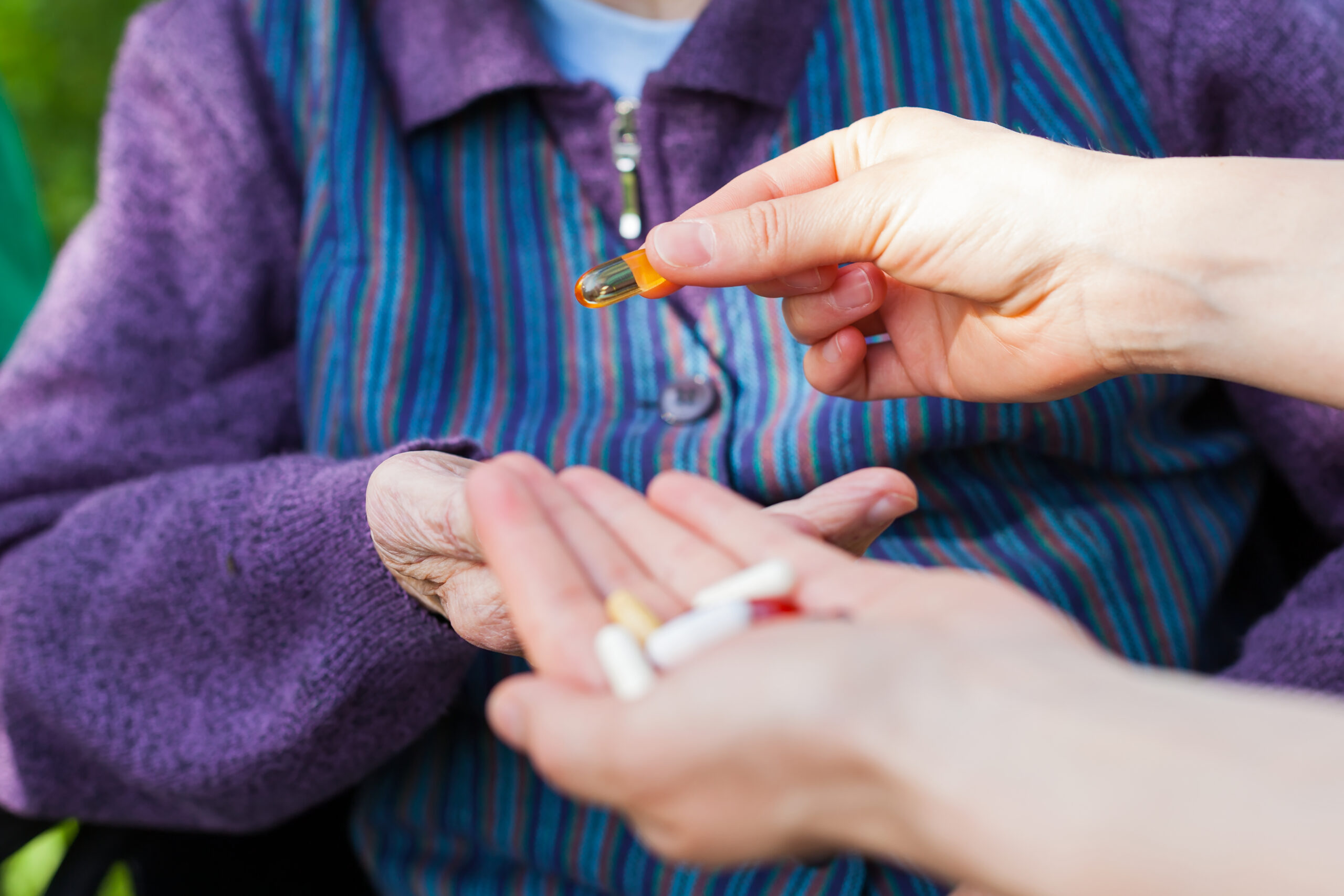 Close up picture of elderly woman's hands receiving medical drugs from caregiver at memory care