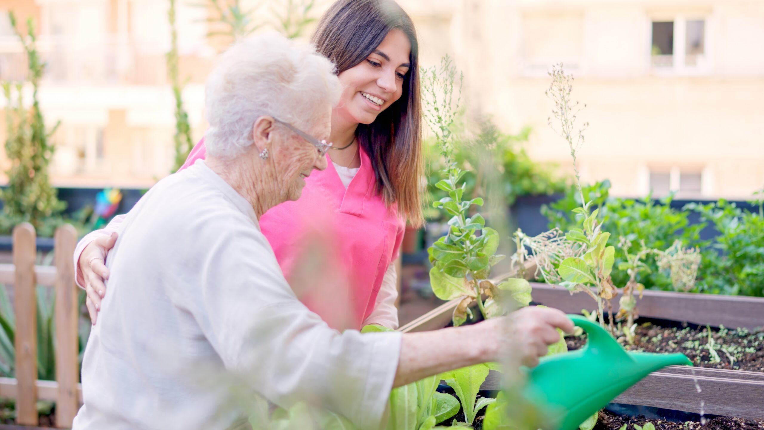 Smiling nurse and senior woman watering plants in memory care.
